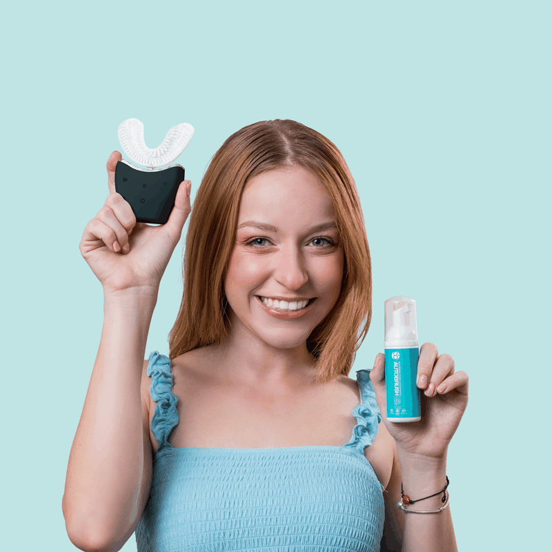 Woman holding Autobrush Sonic Pro electric U-shaped toothbrush and toothpaste bottle against light blue background