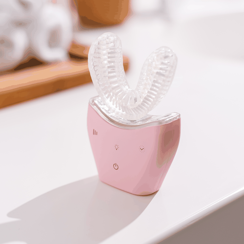 Pink Autobrush Sonic Pro U-shaped electric toothbrush with silicone bristles on a white countertop.