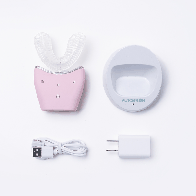 Autobrush Sonic Pro U-shaped electric toothbrush with silicone bristles, charging dock, USB cable, and power adapter in pink and white.