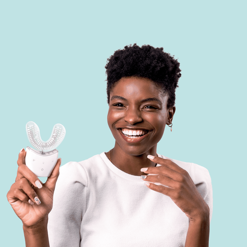 Smiling woman holding Autobrush Sonic Pro U-shaped electric toothbrush with silicone bristles against blue background